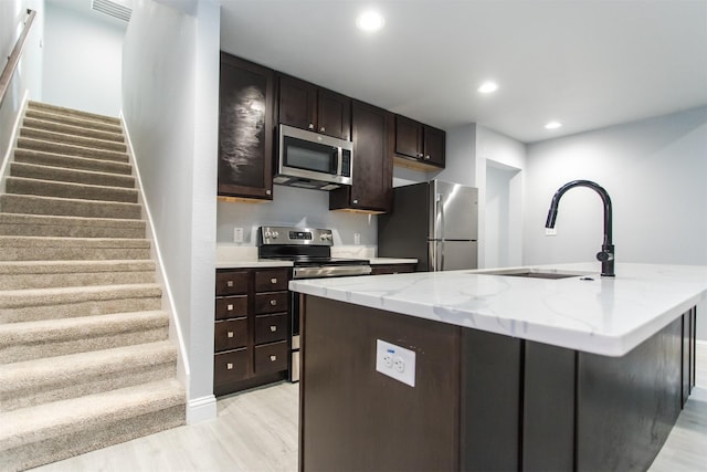 kitchen featuring sink, light hardwood / wood-style flooring, appliances with stainless steel finishes, light stone counters, and an island with sink