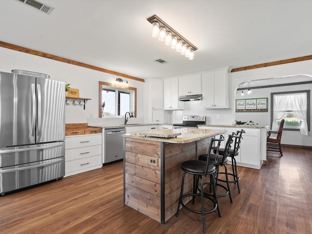 kitchen with stainless steel appliances, white cabinetry, a kitchen island, and a healthy amount of sunlight