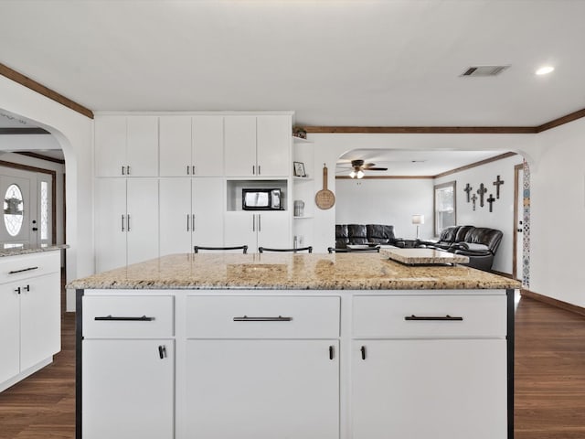 kitchen with crown molding, a center island, dark hardwood / wood-style flooring, ceiling fan, and white cabinets