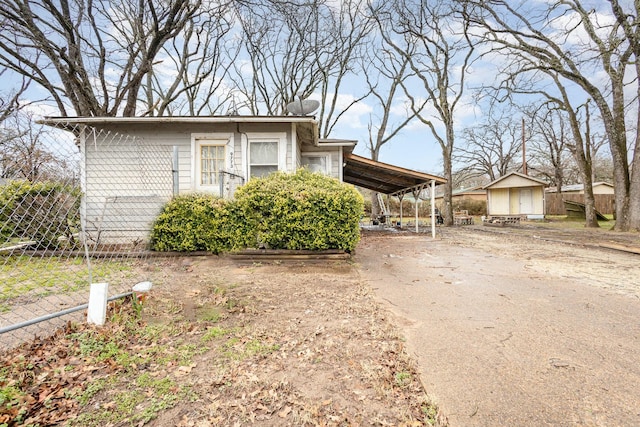 view of front of house with an attached carport, fence, concrete driveway, a storage shed, and an outdoor structure