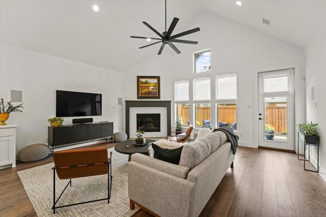 living area with ceiling fan, high vaulted ceiling, a fireplace, baseboards, and dark wood finished floors