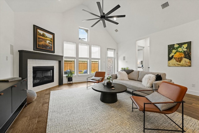 living room with dark wood finished floors, visible vents, a glass covered fireplace, ceiling fan, and high vaulted ceiling