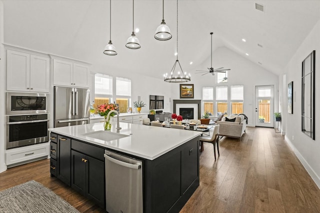 kitchen with appliances with stainless steel finishes, open floor plan, a kitchen island with sink, light countertops, and a sink