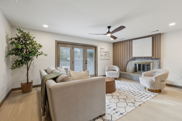 living room with french doors, ceiling fan, a premium fireplace, and light hardwood / wood-style floors