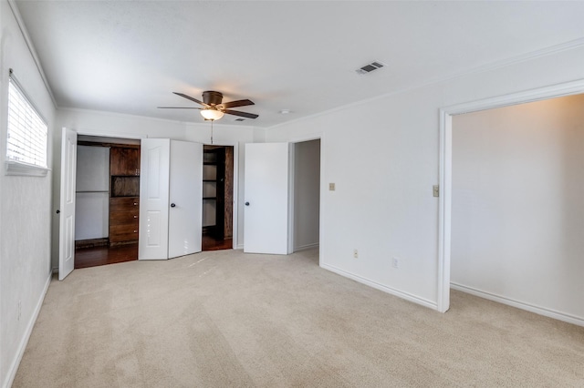 unfurnished bedroom with ceiling fan, ornamental molding, light carpet, and two closets