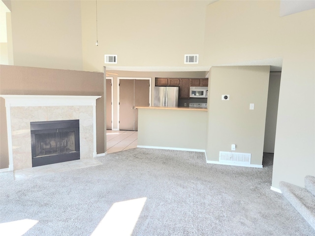 unfurnished living room featuring a towering ceiling, a fireplace, and light colored carpet