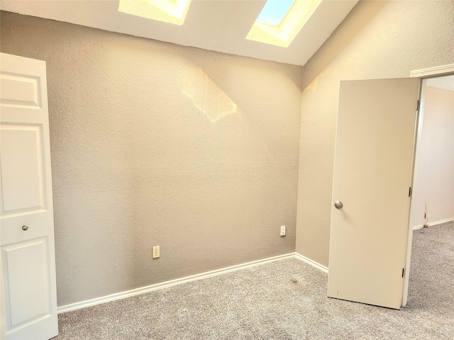 carpeted empty room featuring lofted ceiling with skylight