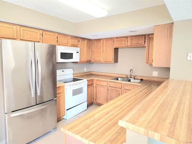 kitchen featuring sink, white appliances, light tile patterned floors, and a textured ceiling