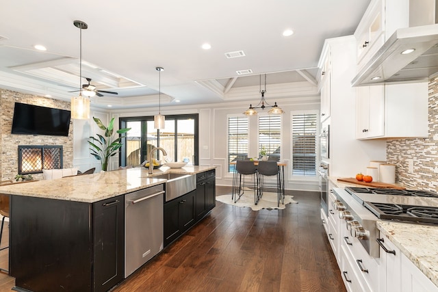 kitchen featuring pendant lighting, sink, a kitchen island with sink, stainless steel appliances, and wall chimney exhaust hood