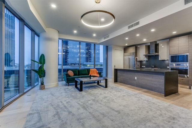 kitchen featuring tasteful backsplash, a kitchen island with sink, built in appliances, light hardwood / wood-style floors, and wall chimney range hood