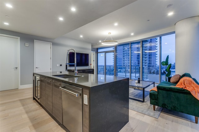 kitchen with dishwasher, sink, dark brown cabinetry, a center island with sink, and light wood-type flooring