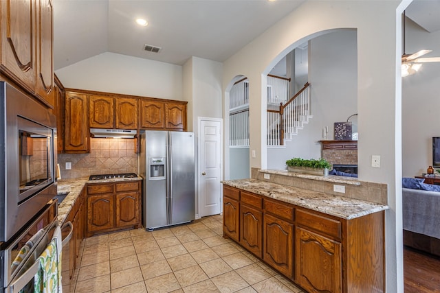 kitchen with lofted ceiling, decorative backsplash, light tile patterned floors, stainless steel appliances, and light stone countertops