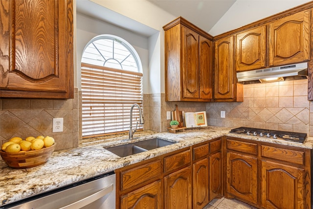 kitchen featuring lofted ceiling, sink, appliances with stainless steel finishes, backsplash, and light stone countertops