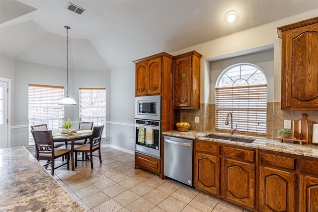 kitchen with vaulted ceiling, appliances with stainless steel finishes, pendant lighting, sink, and light stone counters