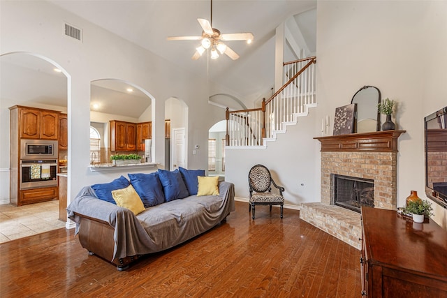 living room with a brick fireplace, high vaulted ceiling, light hardwood / wood-style floors, and ceiling fan