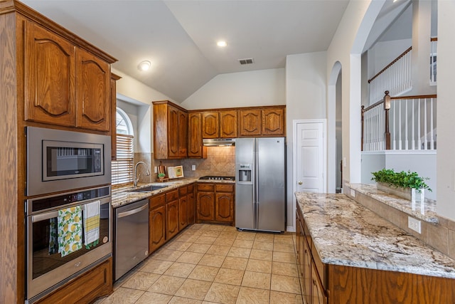 kitchen featuring lofted ceiling, sink, light stone counters, appliances with stainless steel finishes, and backsplash