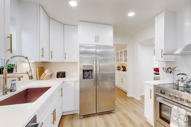 kitchen with stainless steel appliances, sink, wall chimney range hood, and white cabinets