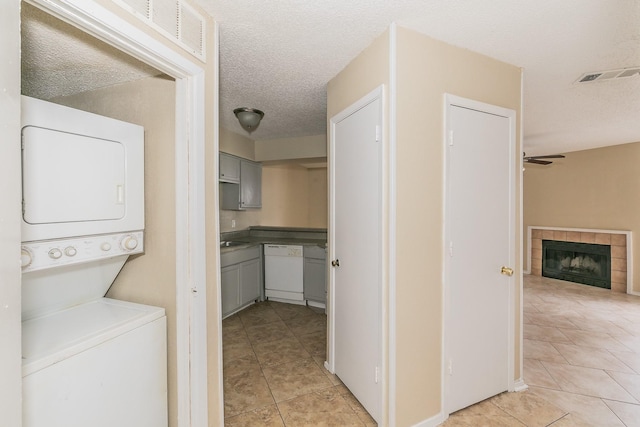 laundry room with light tile patterned floors, ceiling fan, stacked washer and clothes dryer, a fireplace, and a textured ceiling