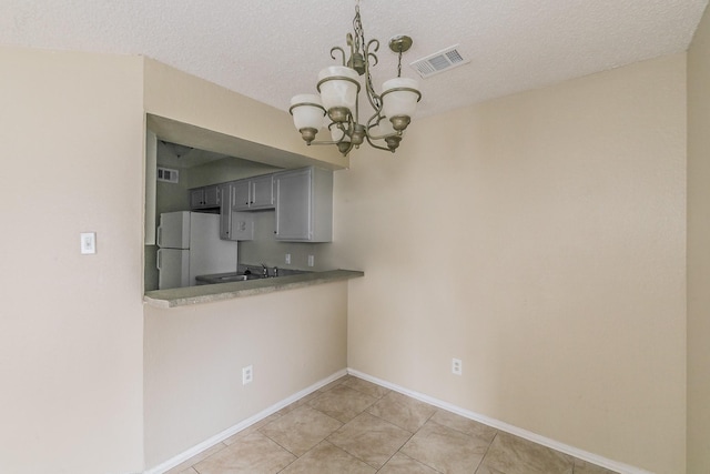 kitchen with white refrigerator, gray cabinets, a textured ceiling, and a notable chandelier