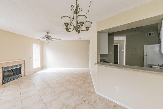 unfurnished living room with light tile patterned flooring, heating unit, a textured ceiling, a tile fireplace, and ceiling fan with notable chandelier