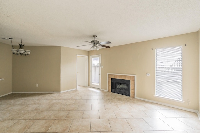 unfurnished living room featuring ceiling fan with notable chandelier, a wealth of natural light, a tile fireplace, and a textured ceiling