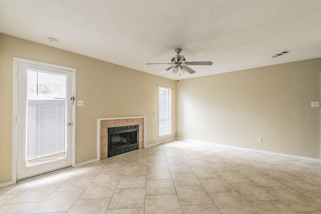 unfurnished living room with ceiling fan, plenty of natural light, a tile fireplace, and a textured ceiling