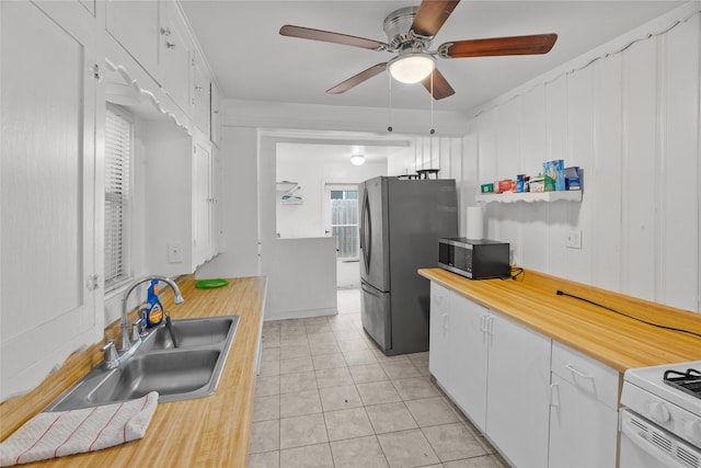 kitchen featuring sink, light tile patterned floors, ceiling fan, appliances with stainless steel finishes, and white cabinetry