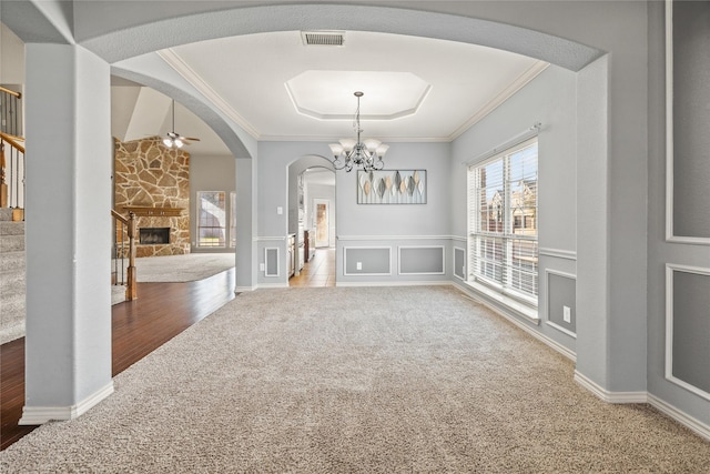 unfurnished dining area featuring crown molding, a stone fireplace, a raised ceiling, and carpet