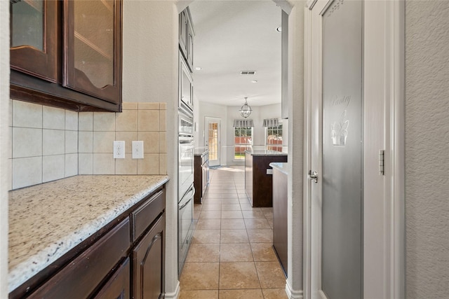 1300 Spanish Needle Trl, Fort Worth, TX 76177 - kitchen featuring decorative backsplash, light tile patterned flooring, dark brown cabinetry, glass insert cabinets, and light stone counters