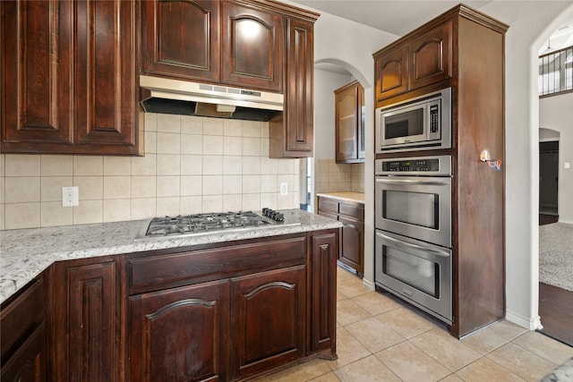 1300 Spanish Needle Trl, Fort Worth, TX 76177 - kitchen featuring light tile patterned floors, stainless steel appliances, under cabinet range hood, backsplash, and arched walkways