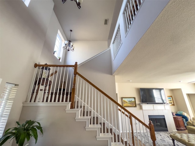 staircase featuring a high ceiling, a tiled fireplace, visible vents, and a notable chandelier