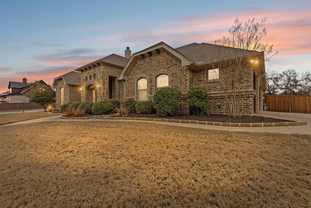 view of front of home with roof with shingles, brick siding, a front lawn, and fence