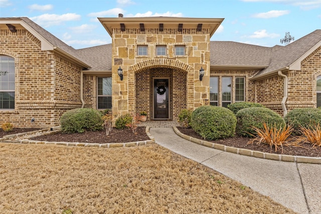 entrance to property with a shingled roof, stone siding, and brick siding