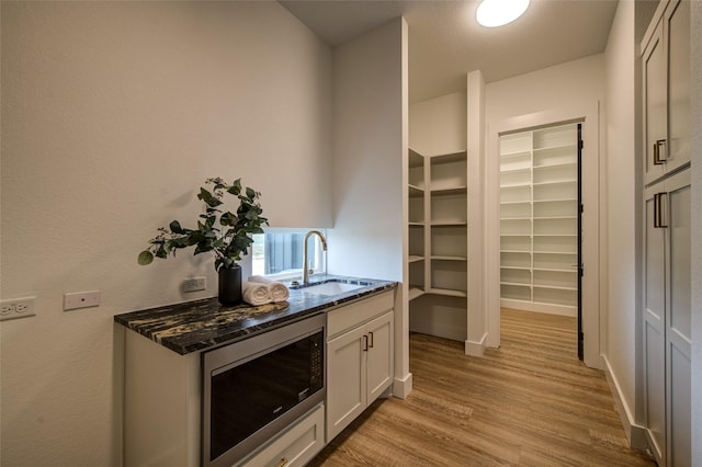 bar featuring stainless steel microwave, light wood-type flooring, and a sink