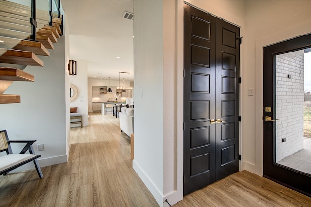 foyer entrance featuring baseboards, visible vents, light wood finished floors, and stairs