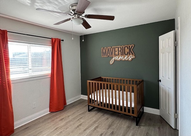 bedroom featuring a ceiling fan, a crib, baseboards, and wood finished floors