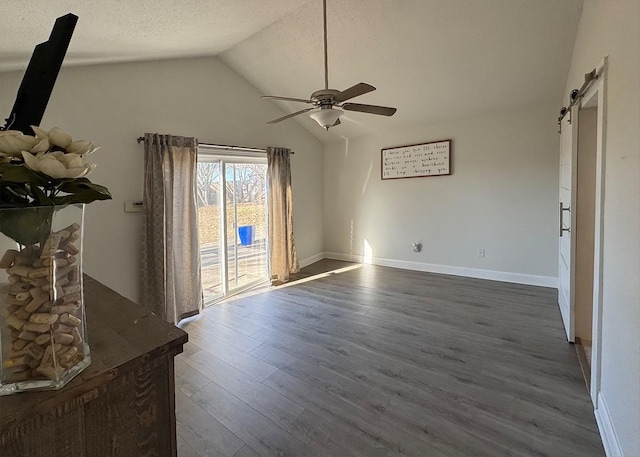 spare room with a barn door, lofted ceiling, ceiling fan, dark wood-style flooring, and a textured ceiling