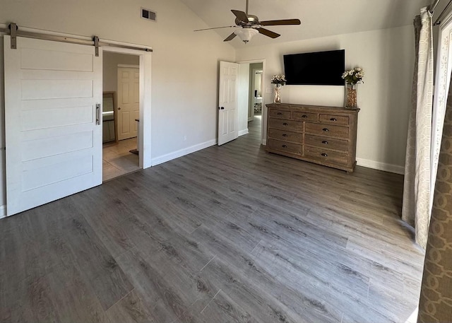 unfurnished bedroom with lofted ceiling, a barn door, dark wood-type flooring, and visible vents