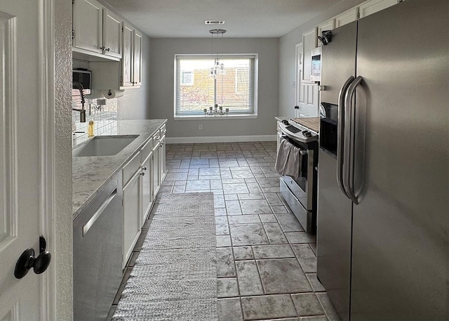 kitchen featuring a sink, white cabinetry, baseboards, appliances with stainless steel finishes, and decorative light fixtures