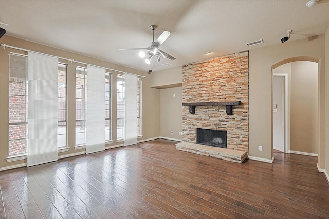 unfurnished living room with dark hardwood / wood-style flooring, a stone fireplace, and ceiling fan