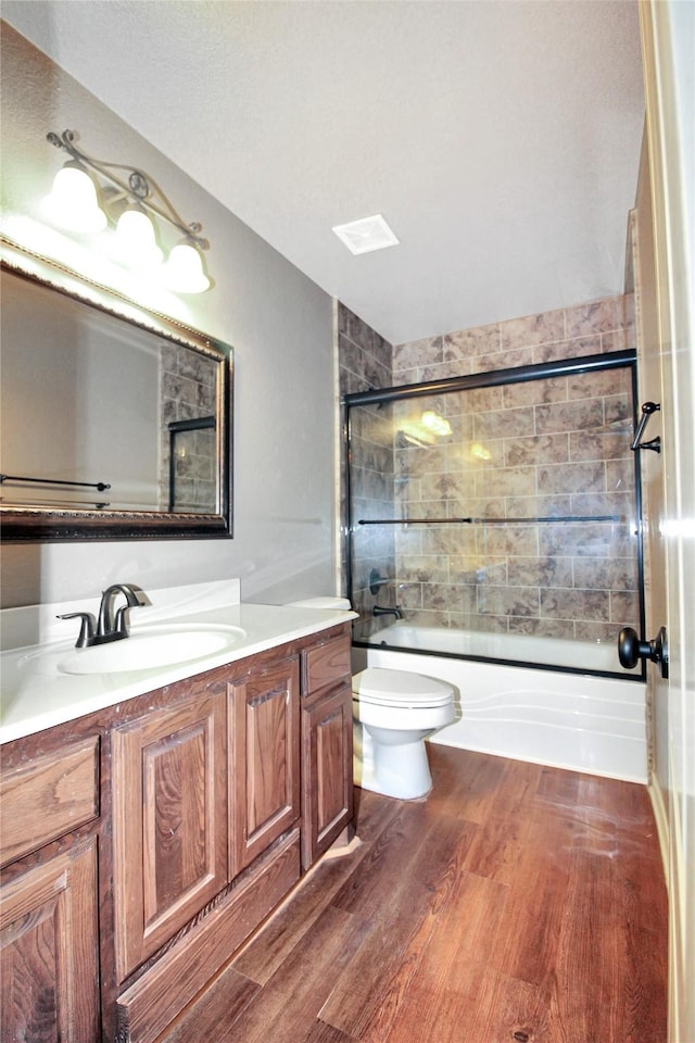 full bathroom featuring hardwood / wood-style flooring, vanity, toilet, and combined bath / shower with glass door