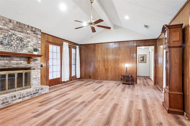 unfurnished living room with lofted ceiling with beams, a textured ceiling, wooden walls, and light hardwood / wood-style floors