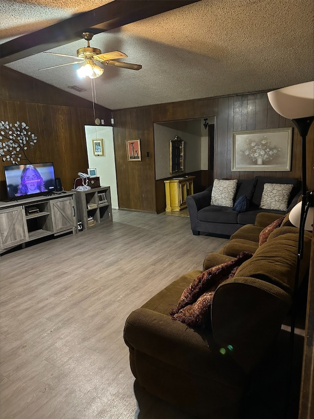 living room featuring ceiling fan, light hardwood / wood-style flooring, vaulted ceiling with beams, and a textured ceiling