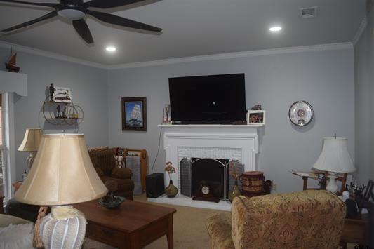 carpeted living room with crown molding, a fireplace, and ceiling fan