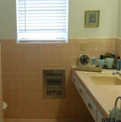 bathroom featuring toilet, sink, heating unit, and tile walls