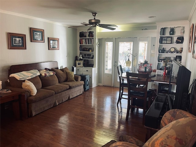 living room with built in features, dark wood-type flooring, ornamental molding, and ceiling fan