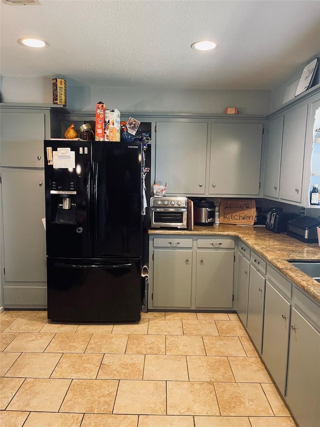 kitchen featuring sink, black fridge with ice dispenser, light tile patterned floors, and a textured ceiling