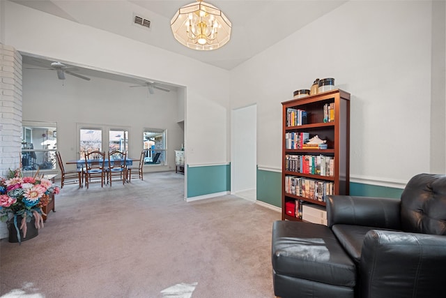 sitting room with ceiling fan with notable chandelier, a towering ceiling, and light colored carpet