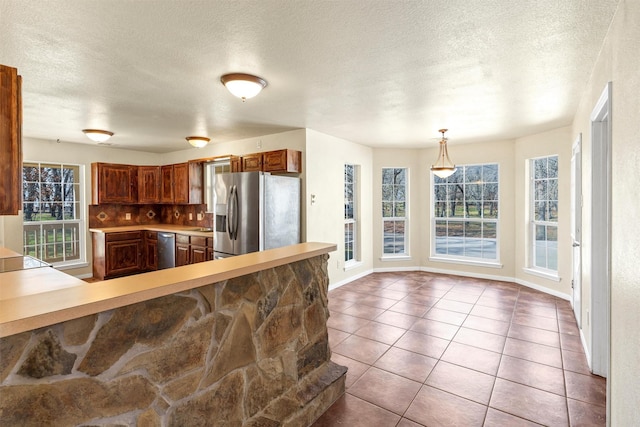 kitchen featuring appliances with stainless steel finishes, tasteful backsplash, hanging light fixtures, light tile patterned floors, and kitchen peninsula