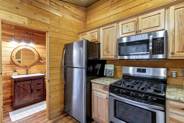 kitchen with appliances with stainless steel finishes, wood walls, light stone countertops, dark hardwood / wood-style flooring, and light brown cabinets